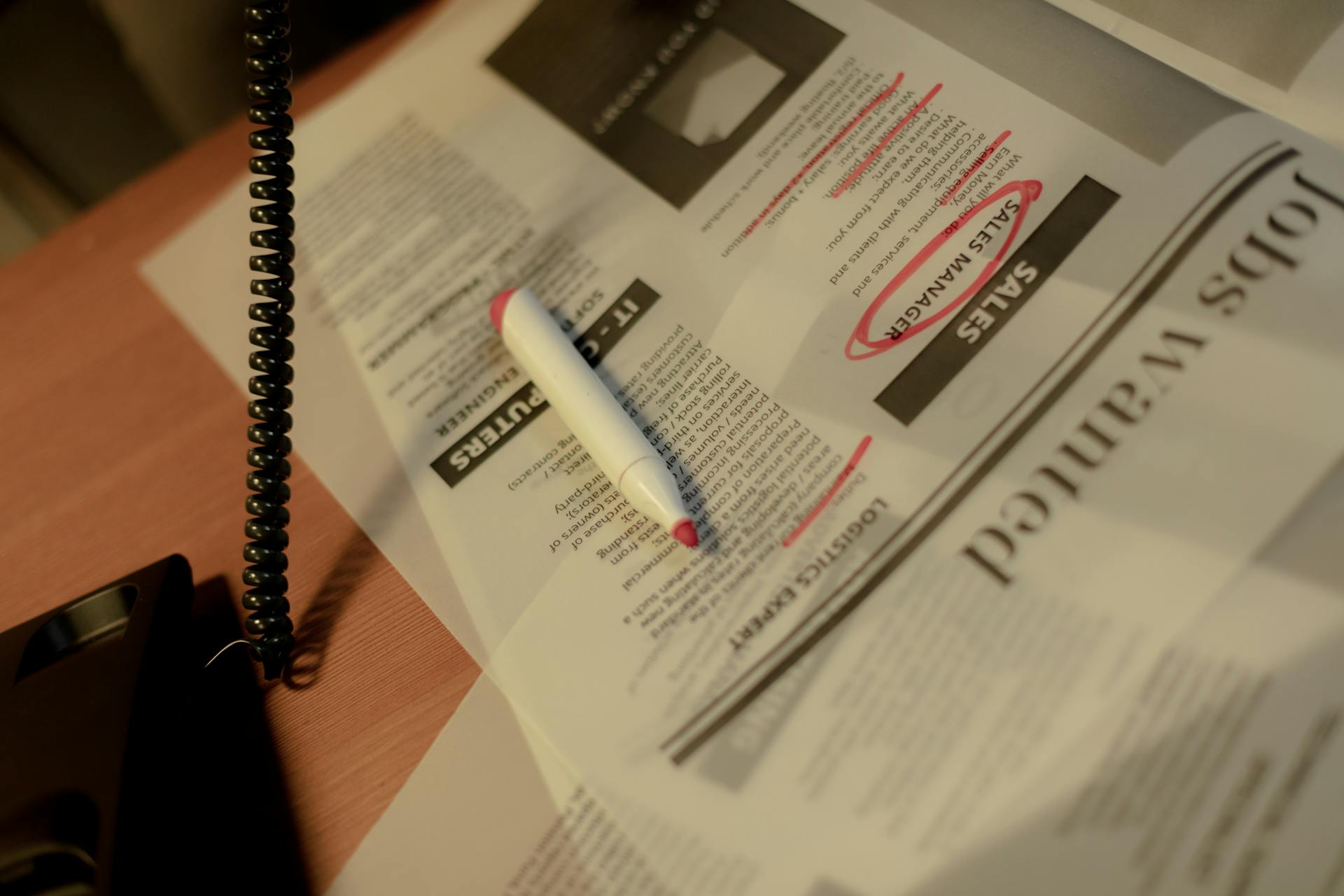 Close-up of a newspaper job section with a red marker and corded phone on a table.