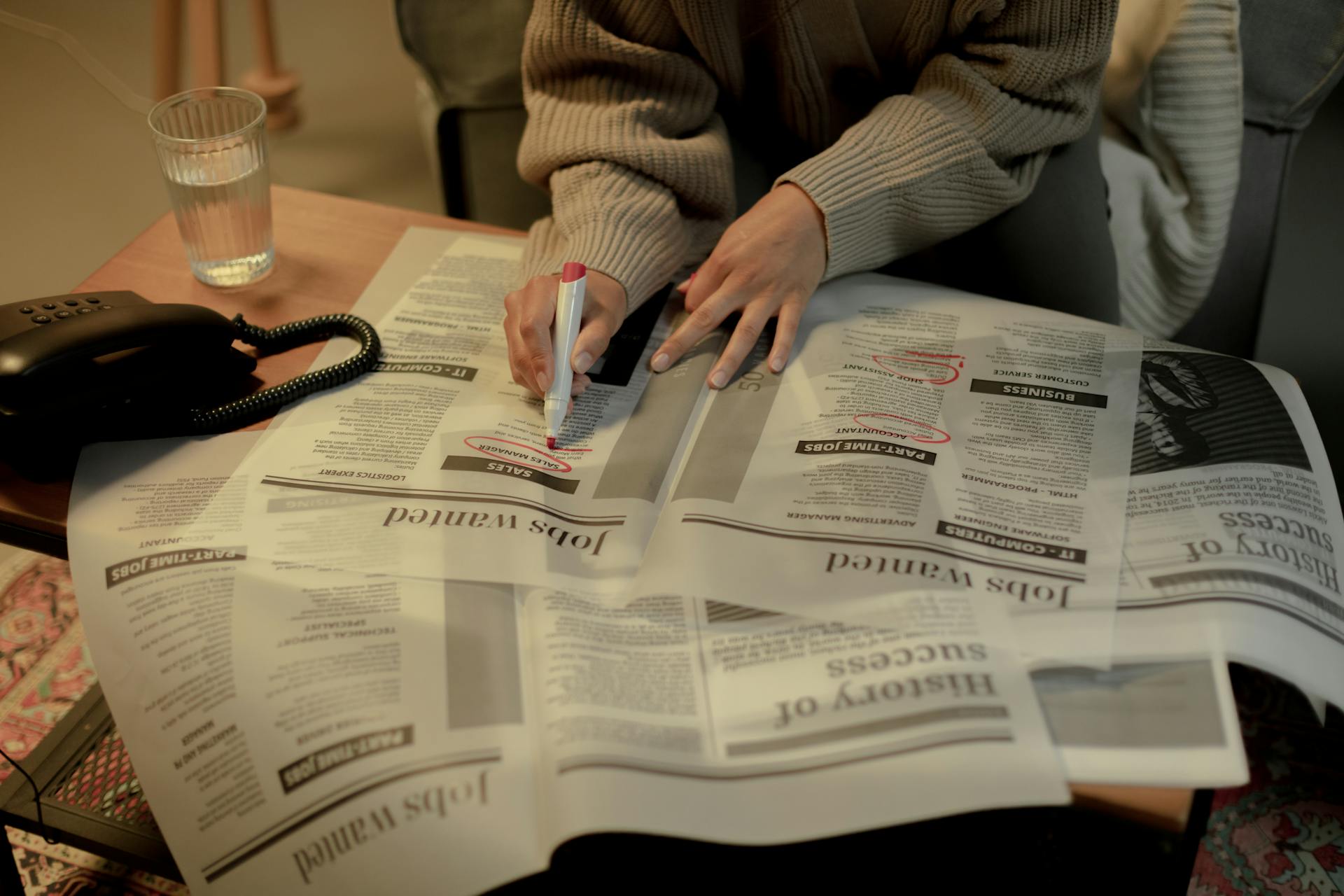 An adult woman marks job listings in a newspaper while sitting indoors, highlighting job search activity.