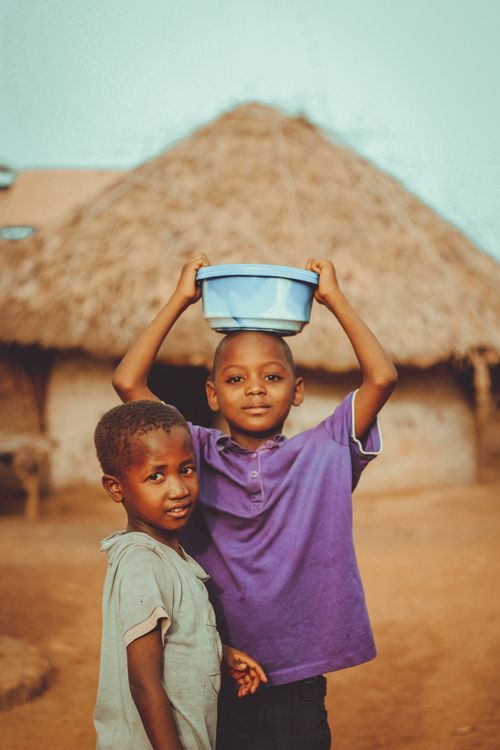 Free Two boys smiling outdoors near a traditional hut in a rural area. Stock Photo