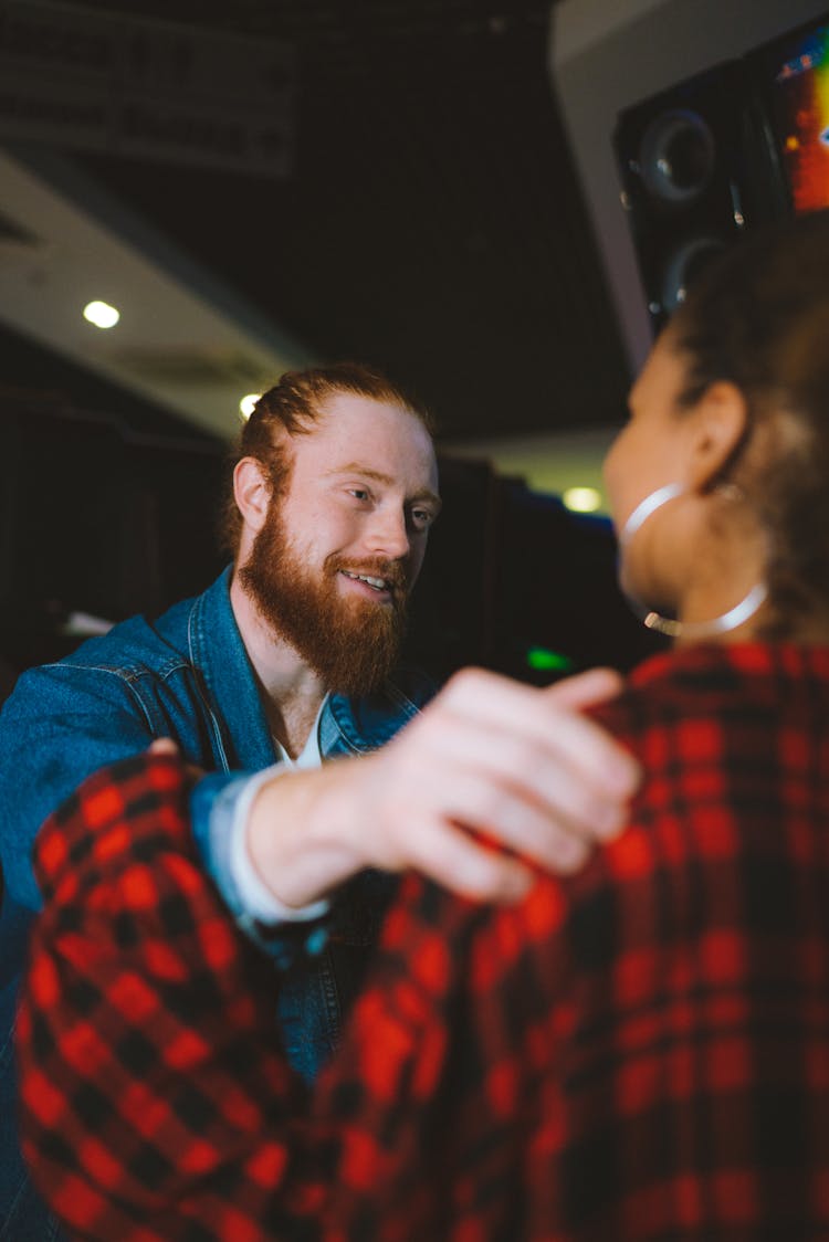 A Bearded Man In Denim Jacket Tapping A Woman's Shoulder In Plaid Long Sleeves