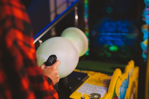 Free Close-up of a person playing an arcade machine with vibrant lights in a gaming arcade. Stock Photo