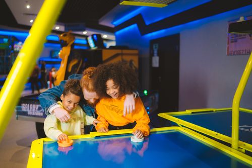 Free Family having fun playing air hockey together at an arcade. Happy moments and smiles captured. Stock Photo