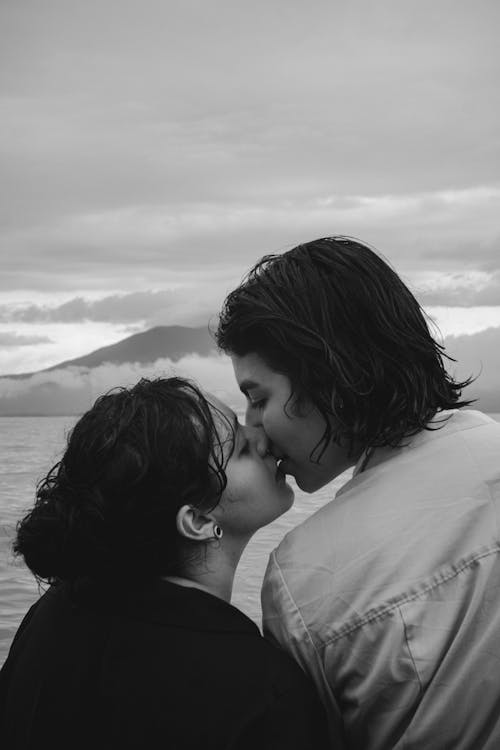 Grayscale Photo of Couple Kissing Near Body of Water