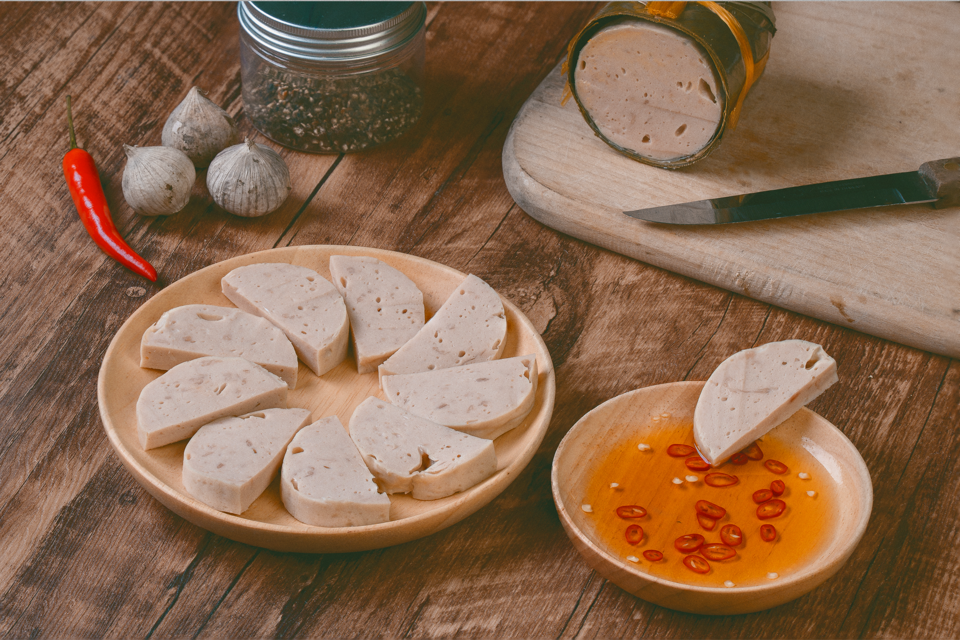 Chả lụa slices with chili, garlic, and dipping sauce on a wooden board.