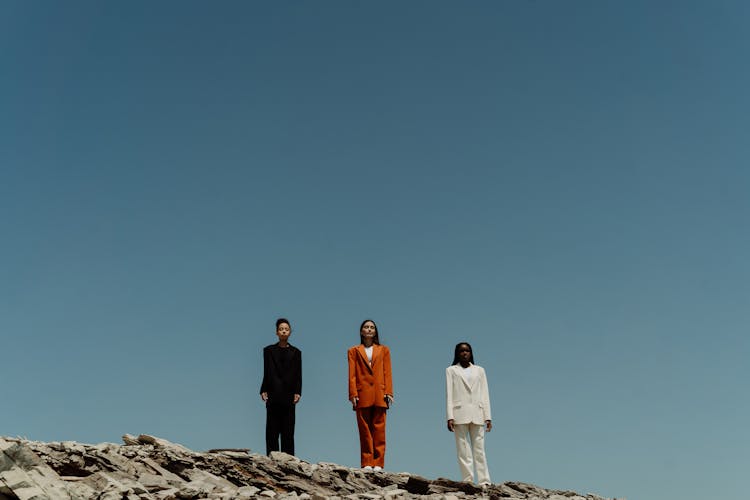 A Low Angle Shot Of Women In Blazer And Pants Standing On The Rock Under The Blue Sky