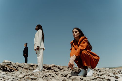 A Woman in Orange Blazer and Pants Sitting on the Rock