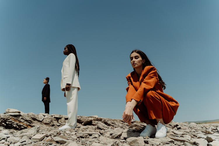 A Woman In Orange Blazer And Pants Sitting On The Rock