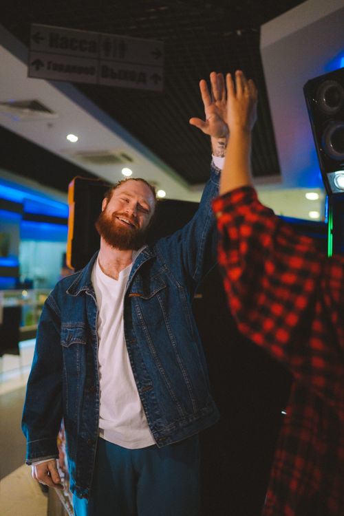 Free Smiling man in denim jacket shares a high five in a vibrant indoor setting. Stock Photo