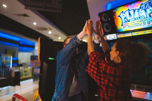 Free Energetic couple having fun at an arcade, sharing a high five and laughter. Stock Photo