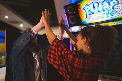 Free A cheerful moment of a couple high-fiving in an arcade environment, celebrating fun and togetherness. Stock Photo