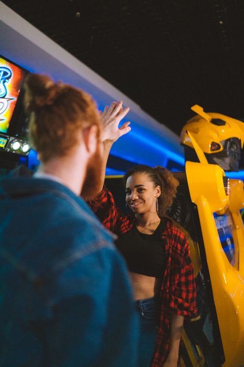 Free Young couple enjoying time at an arcade, smiling and giving high five. Stock Photo