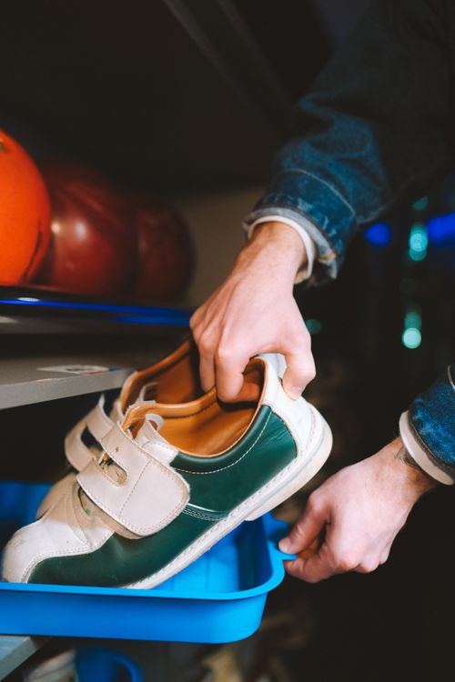 Free Close-up of hands retrieving bowling shoes from a plastic tray indoors. Stock Photo