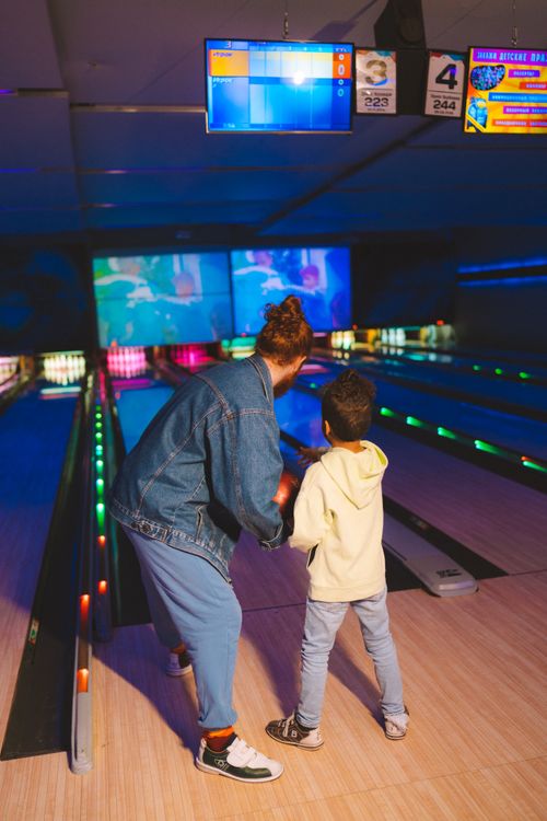 Free Adult and child enjoying a fun night at the bowling alley with vibrant, colorful lights. Stock Photo
