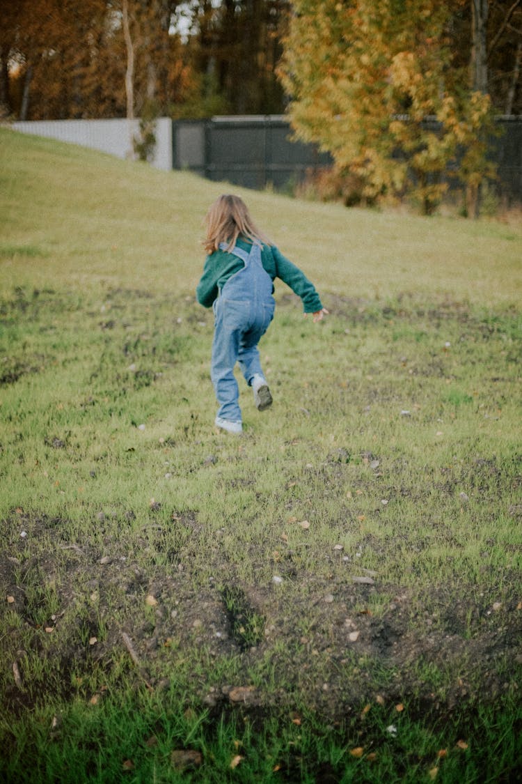 Back View Of A Little Girl Running On A Field