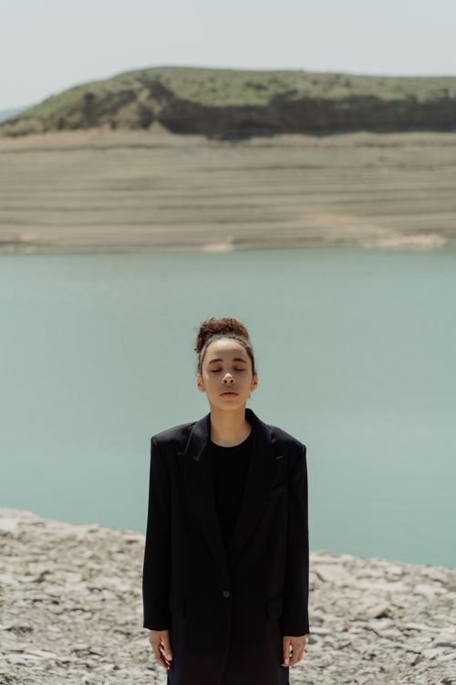 Free Woman in black blazer standing peacefully by a tranquil lake. Stock Photo