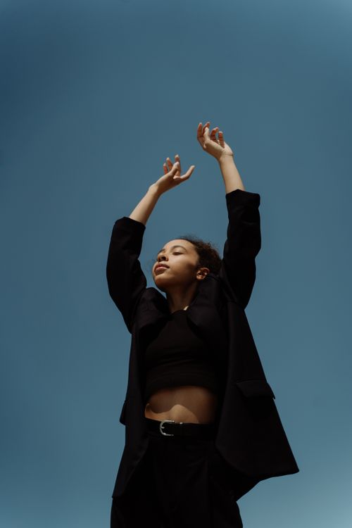 Free Low angle photo of a confident woman raising her hands against a vibrant blue sky. Stock Photo