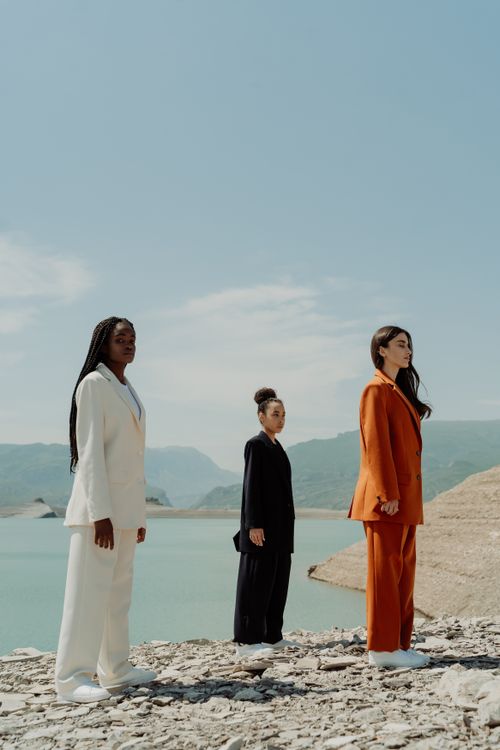 Free Three women in stylish suits pose by a stunning lakeside, showcasing elegance and diversity. Stock Photo