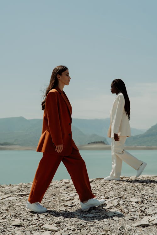 Women Wearing Suits in Different Colors Walking near a Body of Water