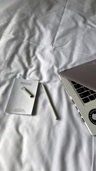 A simple and clean workspace setup featuring a laptop, notebook, and pen on white bedding.