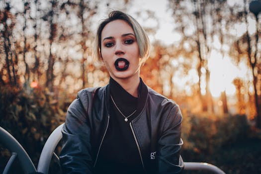 Stylish young woman with striking lipstick sits outdoors amidst fall foliage.