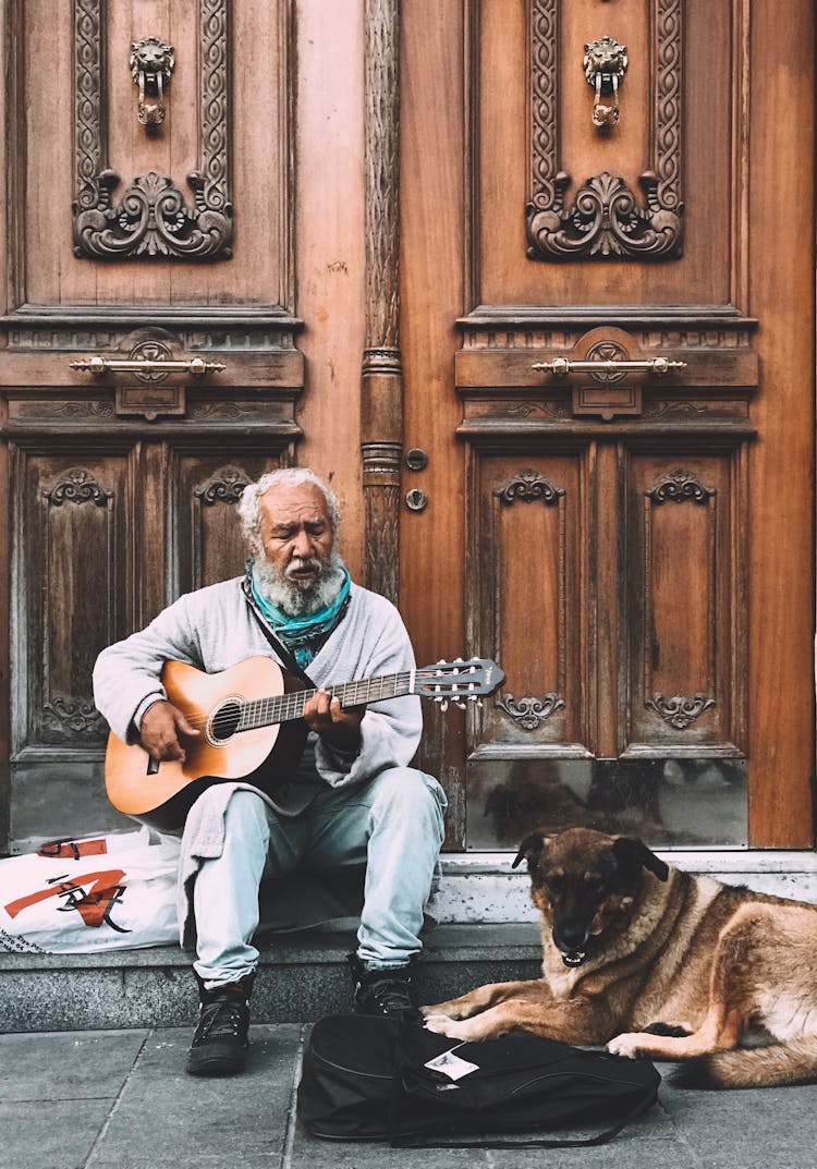 A Dog Lying Down Near A Man Playing A Guitar 