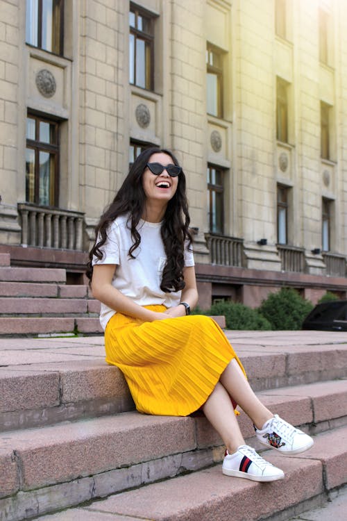 흰색 셔츠와 갈색 콘크리트 벽돌 계단에 앉아 노란색 치마를 입고 여자