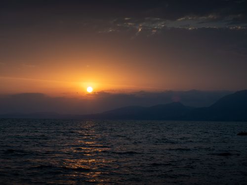 Free Beautiful sunset over the ocean with a silhouette of distant mountains under a dramatic sky. Stock Photo