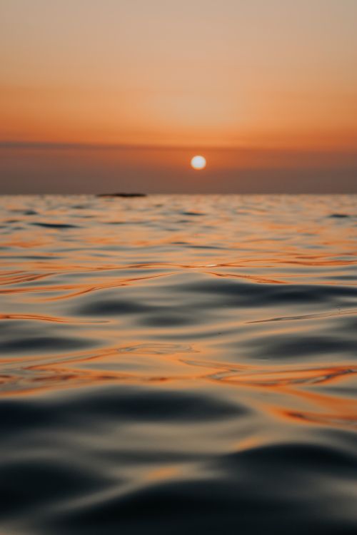 Free A tranquil seascape at sunset with soft water ripples and warm golden tones. Stock Photo