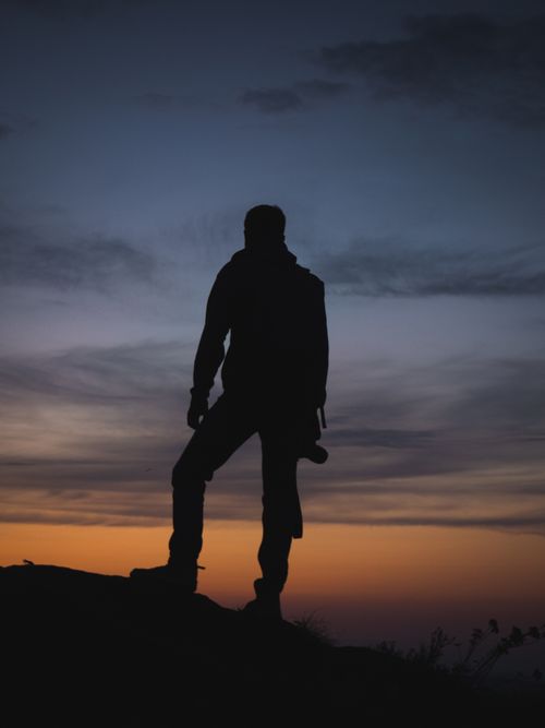 Free A lone silhouette of a man standing on a hill against a vivid sunset sky. Stock Photo