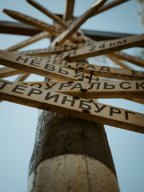 Low-angle view of a wooden signpost with Cyrillic text against a clear blue sky.