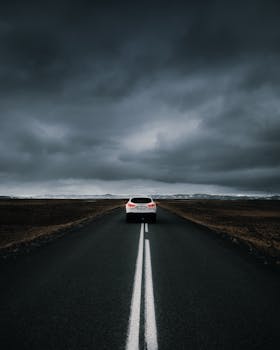 Moody and dramatic road trip in Iceland featuring a car on an open road under dark, cloudy skies.
