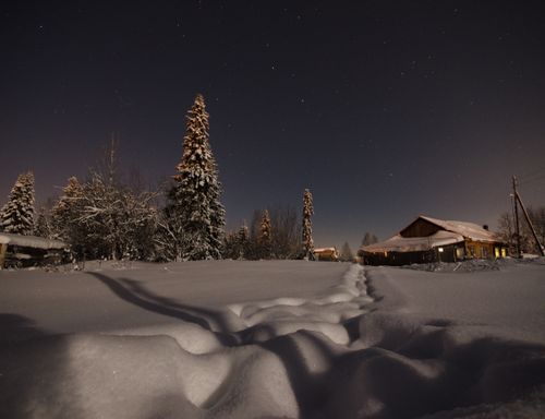 Free Capture of a serene night sky over a snow-covered cabin in a winter landscape. Stock Photo
