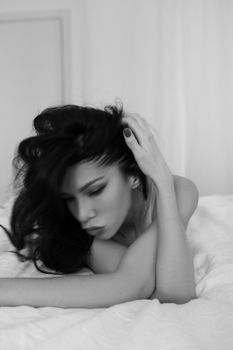 Artistic black and white portrait of a woman lying on a bed, exuding relaxation.