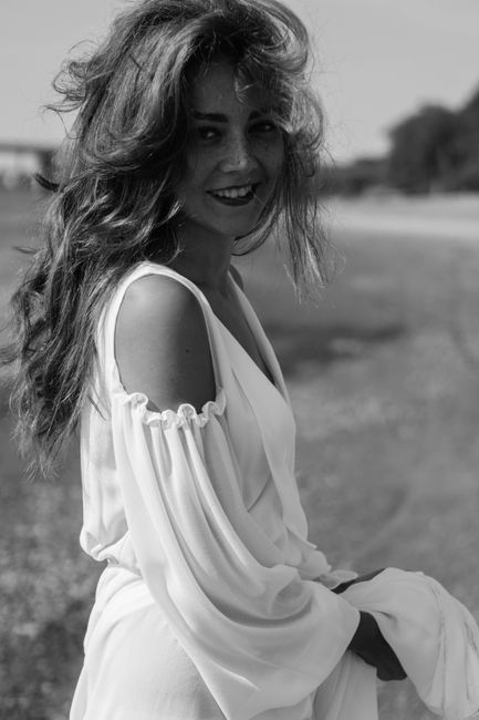 Elegant woman in white dress laughing, captured outdoors in black and white.