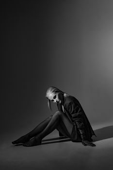 Striking black and white studio portrait of a woman sitting on the floor, exuding elegance and mystery.