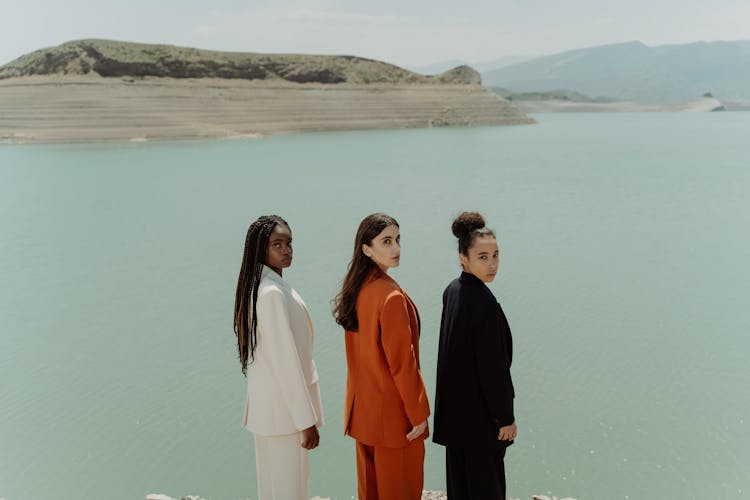 Women In Blazer And Pants Standing Near The Body Of Water While Looking Over Shoulder