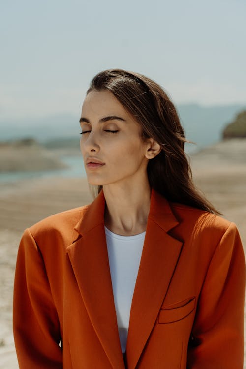 Young Woman in an Elegant Orange Jacket Standing Outside with Eyes Closed