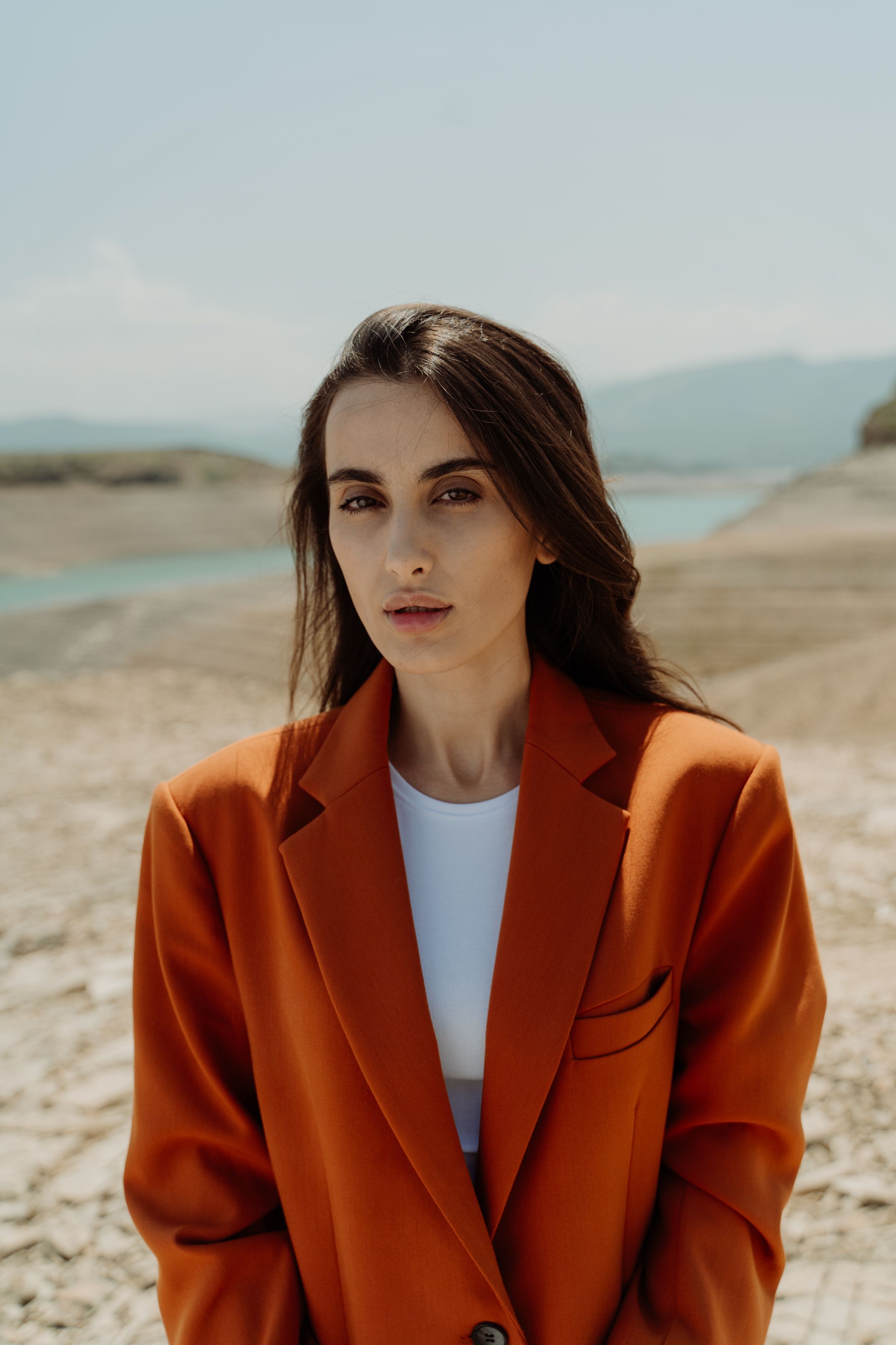 Portrait of a woman in an orange blazer standing near a beach on a sunny day.