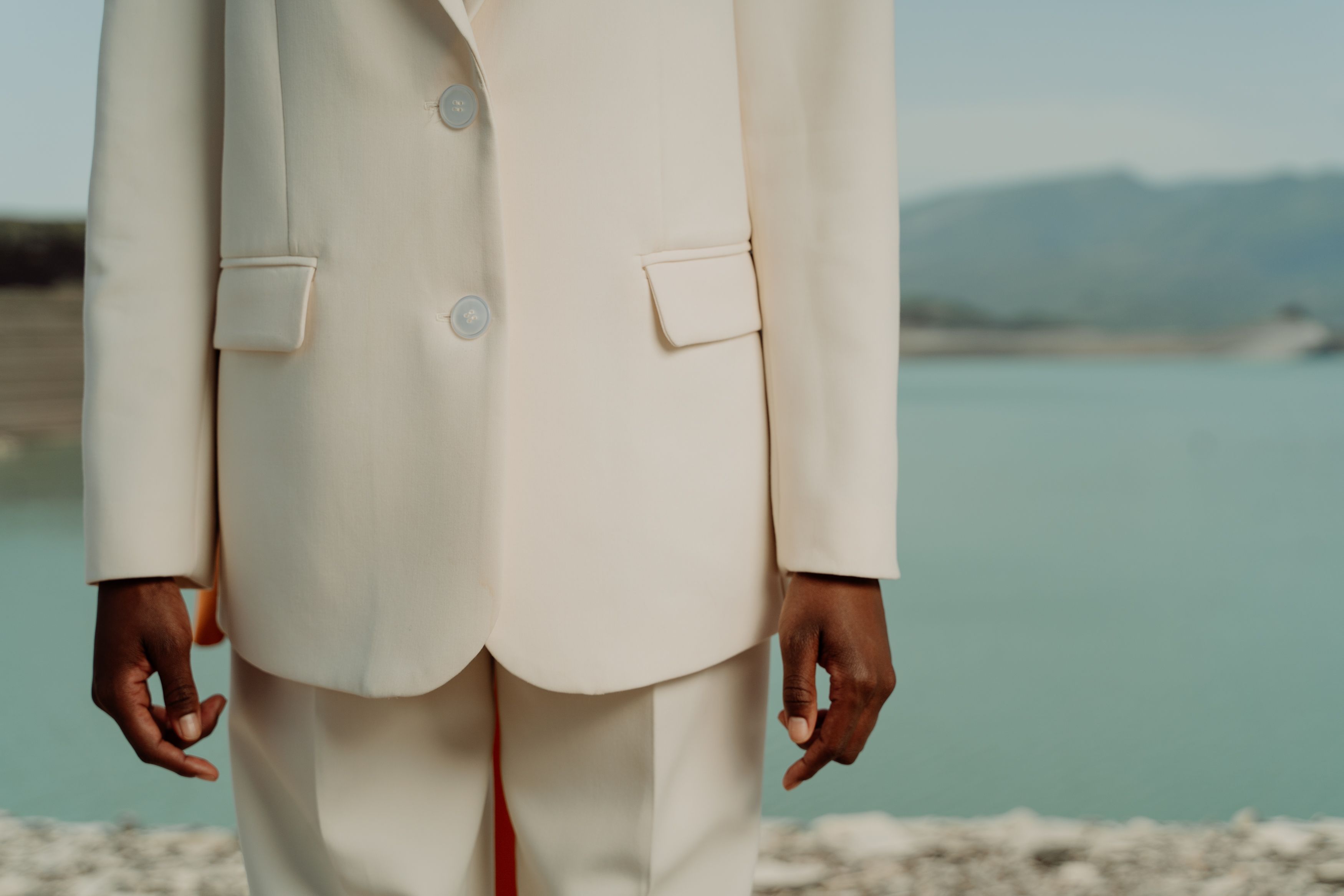 Person in an elegant white suit standing by a tranquil waterside — understated quiet luxury fashion