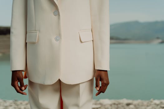 Close-up of a person in a white suit standing by a tranquil waterside.