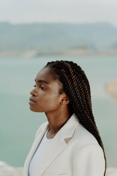 Sophisticated portrait of a black woman in a white blazer by a serene sea.