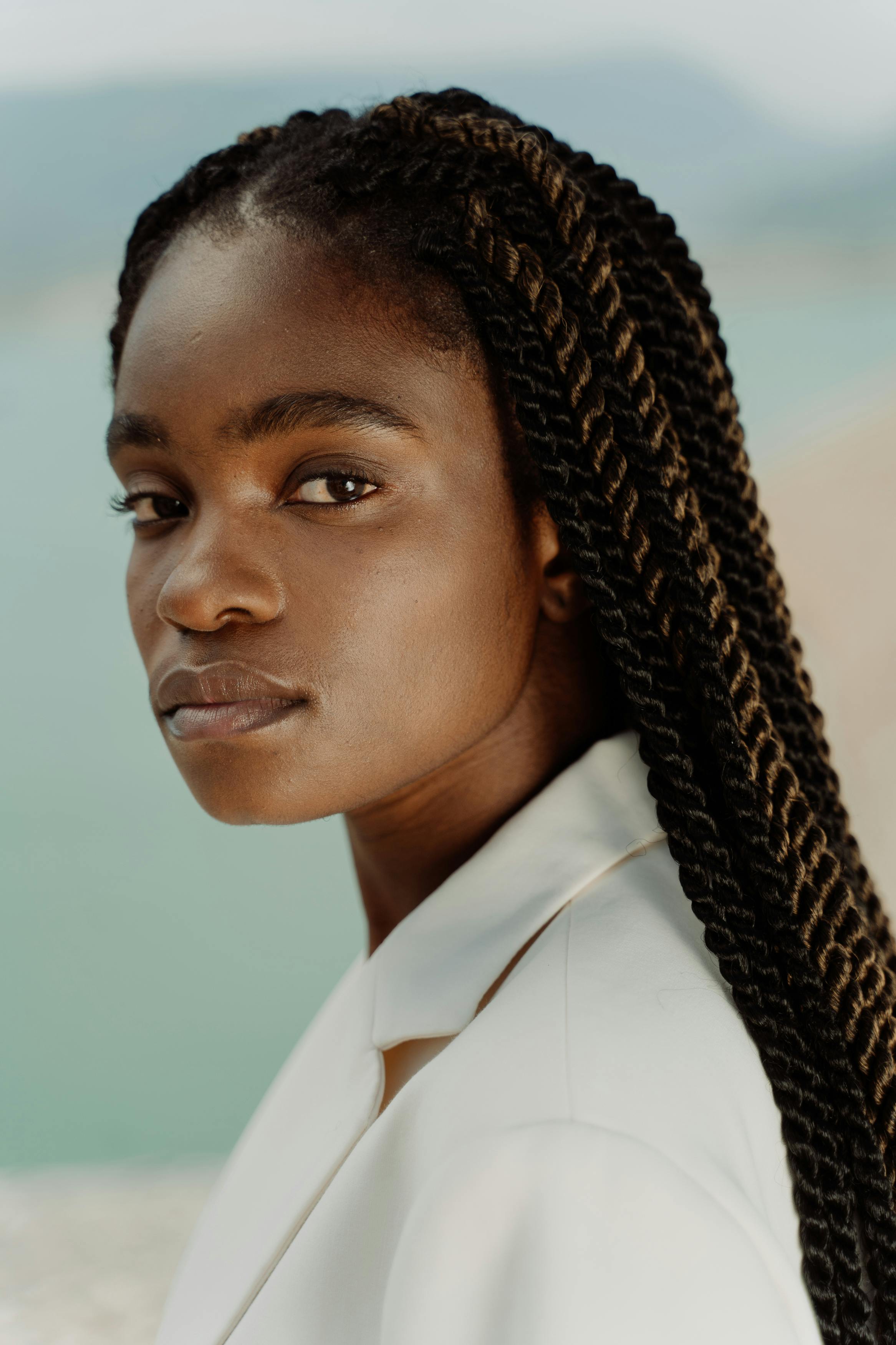 Elegant portrait of a woman in a white blazer with braided hair, captured outdoors.