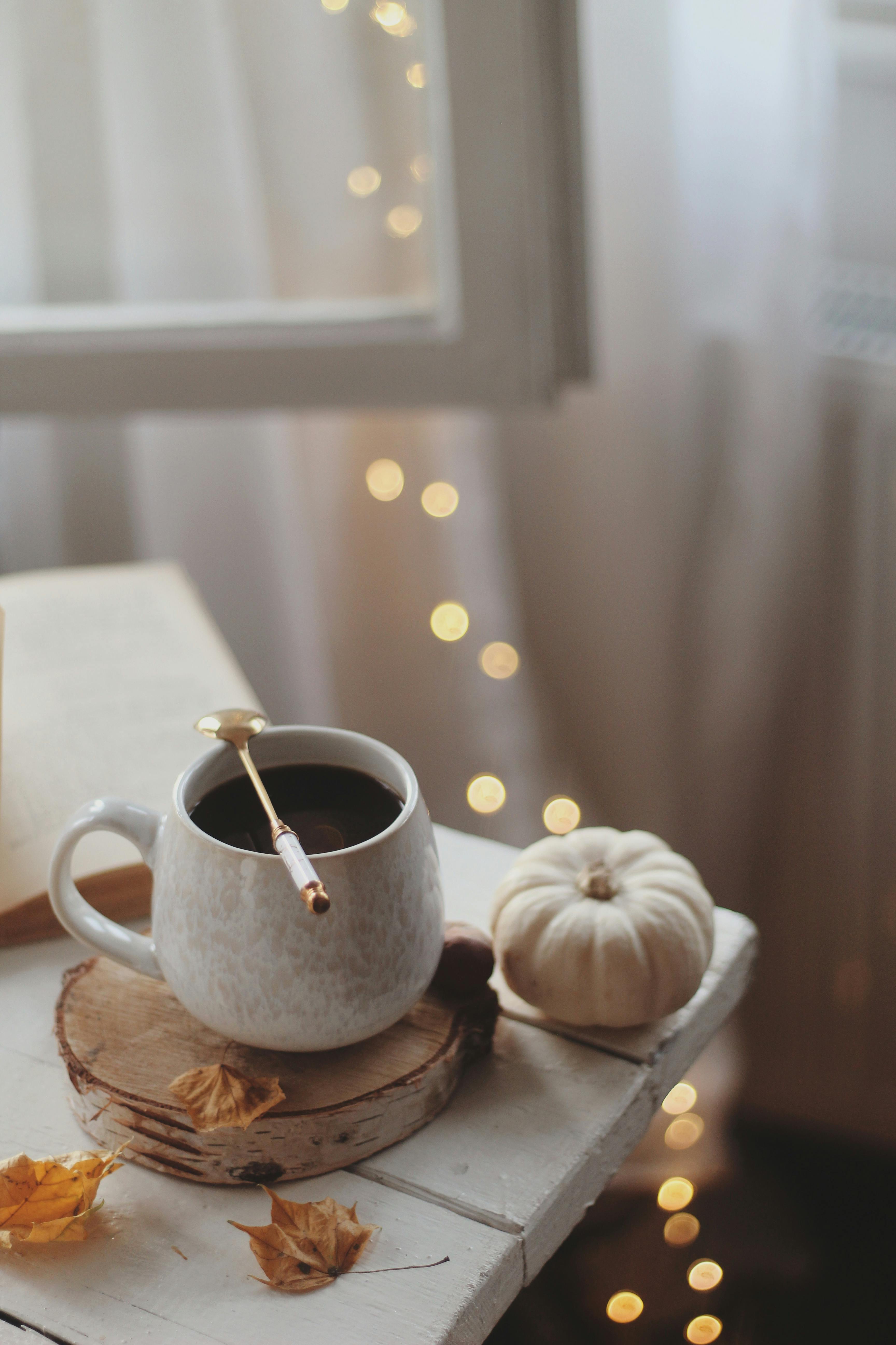 Inviting autumn scene with coffee, pumpkin, and leaves on a rustic table indoors.