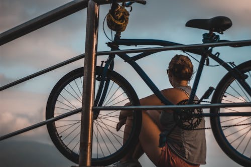 Mujer En Camiseta Sin Mangas Gris Sentada Junto A La Bicicleta Cruiser Negra