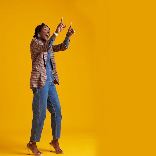 Free A Woman in Plaid Blazer and Denim Jeans Standing while Raising Her Hands Stock Photo