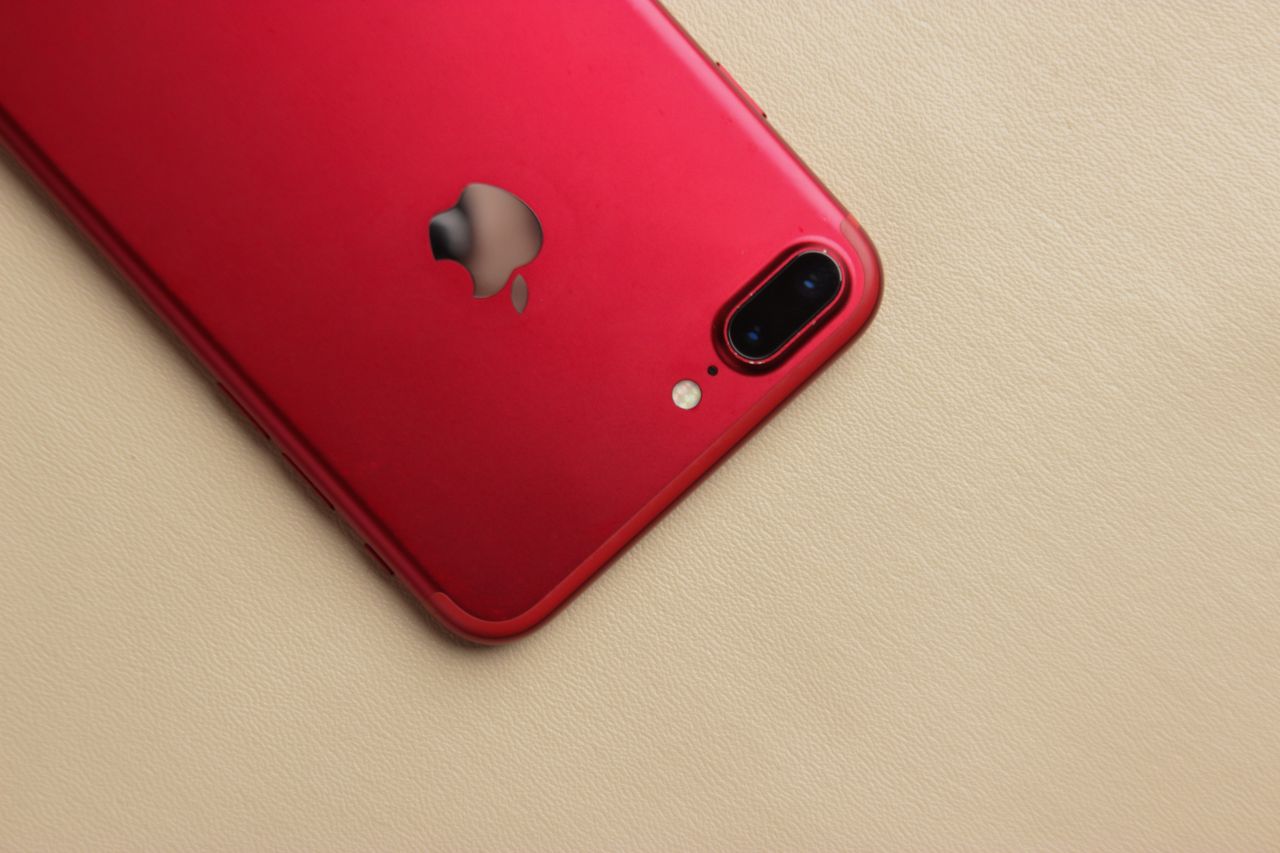 a vibrant red smartphone with a reflective logo on a neutral beige bac