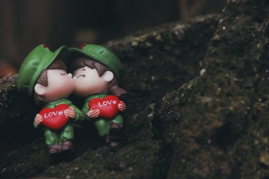 Close-up of toy soldier figures kissing with red heart labeled 'Love' on rock.