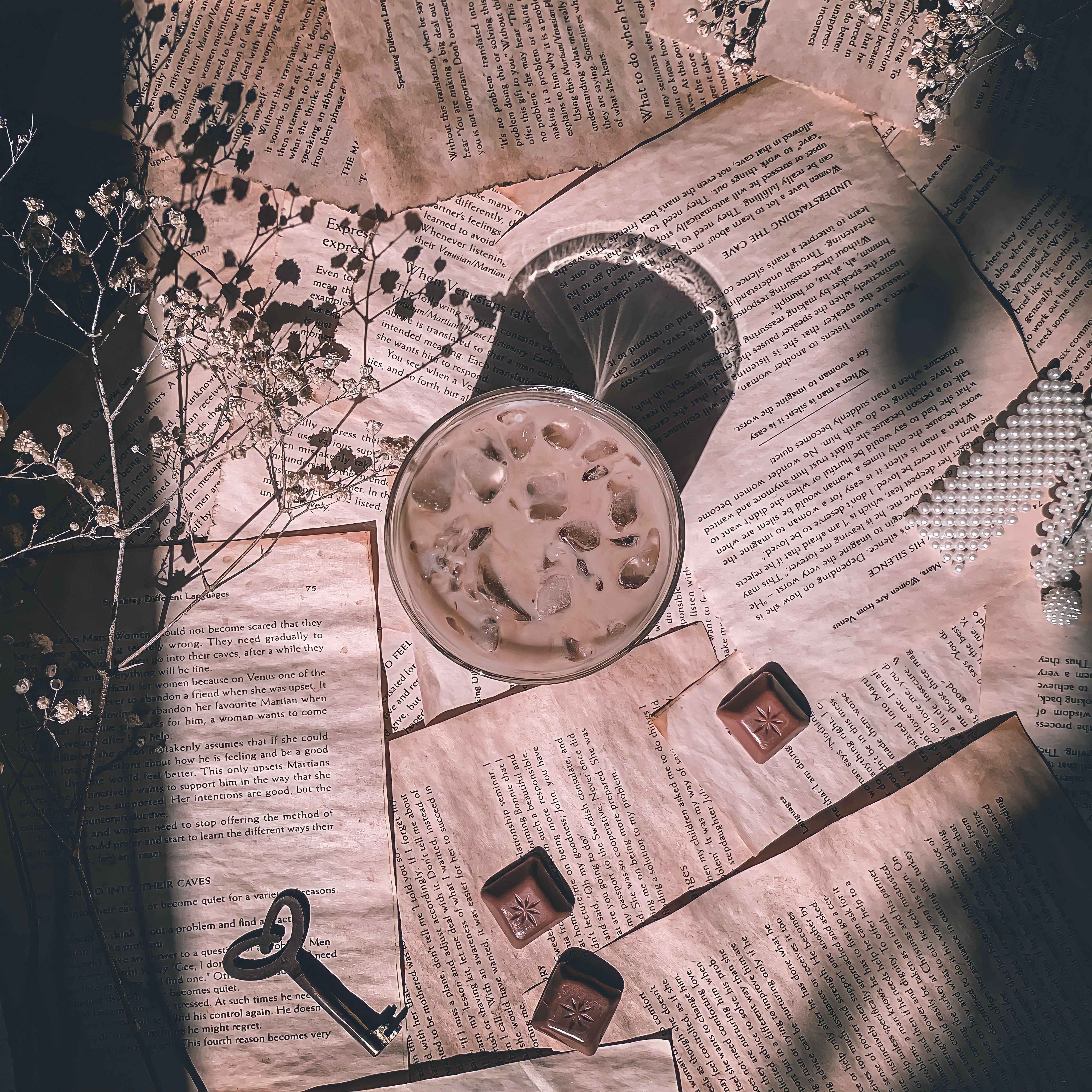 A top view of iced coffee surrounded by vintage papers, flowers, and chocolates.
