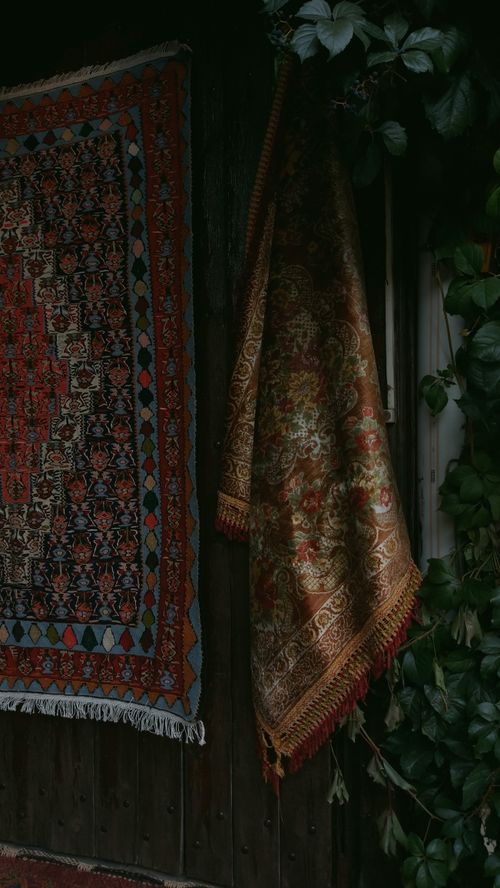Free Intricately designed rugs hanging on a vintage wall, framed by lush green foliage. Stock Photo