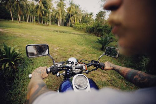 Free A tattooed man on a motorbike explores a tropical area with palm trees, capturing the adventure of motorcycle riding. Stock Photo